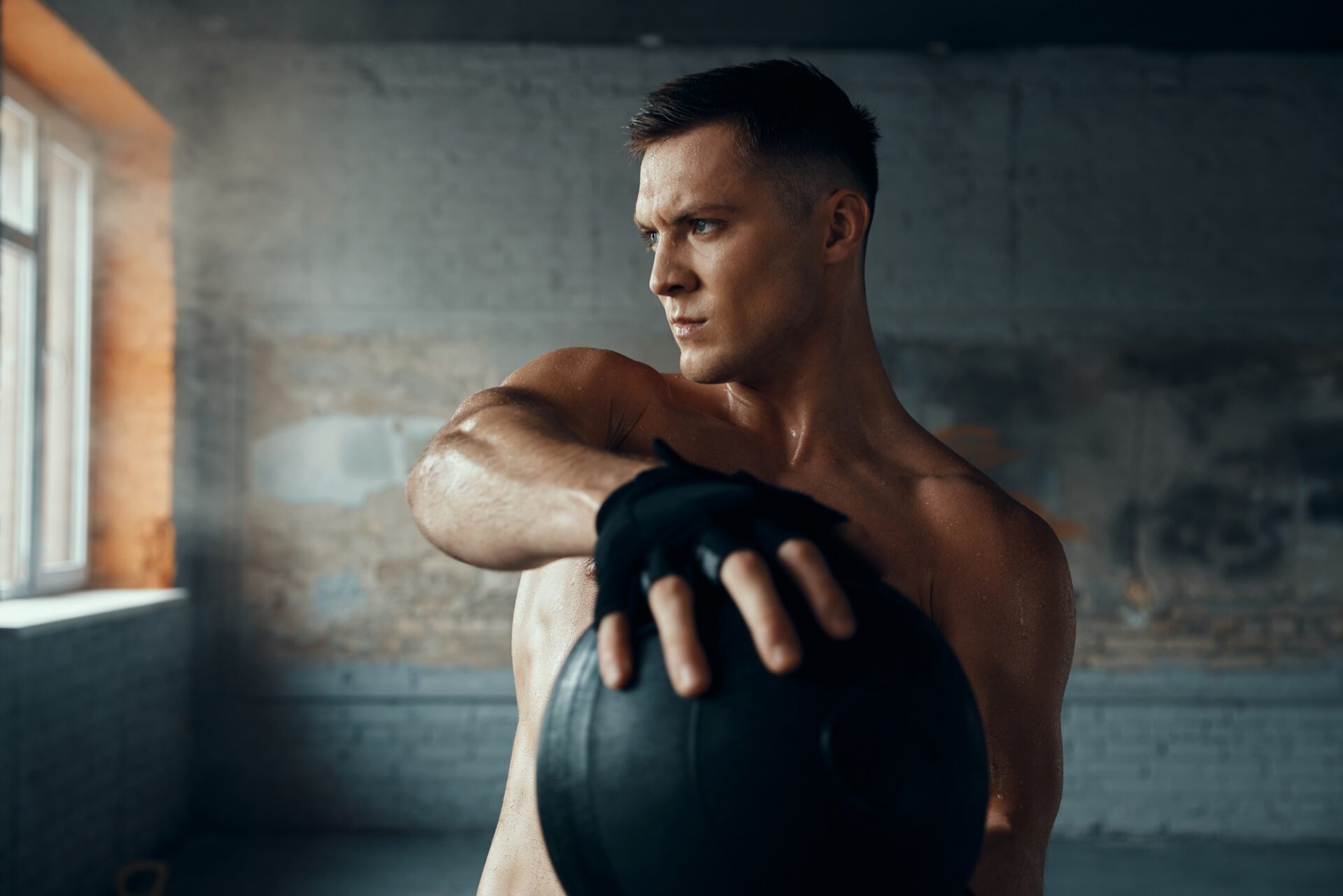 Muscular young man looking concentrated while exercising with medicine ball in gym